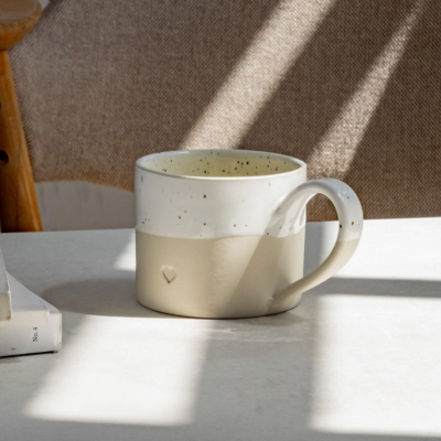 Caneca bicolor de cerâmica com coração em relevo sobre mesa branca com sombra