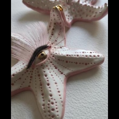 Objetos decorativos em forma de estrelas-do-mar cor de rosa com textura pontilhada sobre superfície branca.