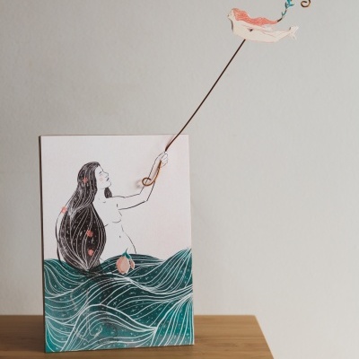 Ilustração de mulher com ondas e figura colorida suspensa em mesa de madeira