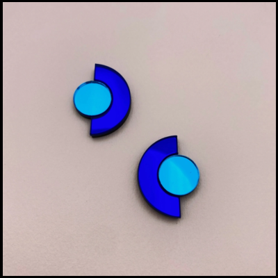 Brincos azuis geométricos com círculo e meia-lua em fundo bege