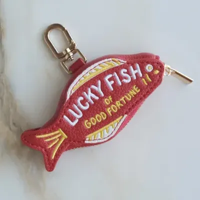 Chaveiro em forma de peixe vermelho com texto bordado e fecho dourado
