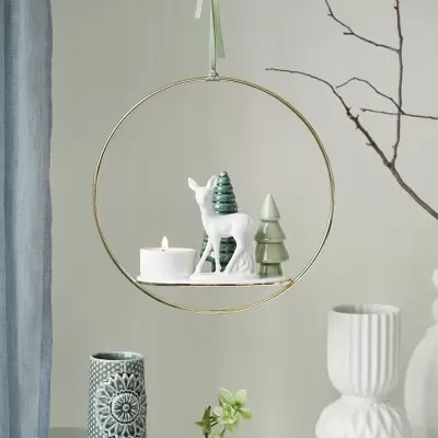 Decoração suspensa com veado branco, árvores verdes e vela dentro de aro metálico dourado