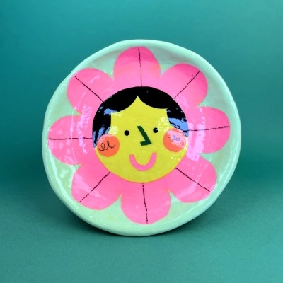 Prato de cerâmica redondo com desenho de flor sorridente em rosa e amarelo