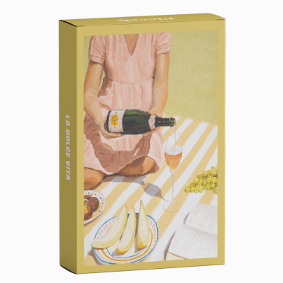 Embalagem amarela com ilustração de pessoa a servir vinho entre frutas e livro