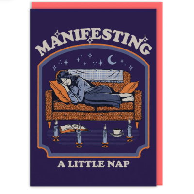 Cartão azul escuro com mulher a dormir num sofá laranja com velas e chávena, texto MANIFESTING A LITTLE NAP