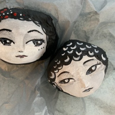 Duas pedras pintadas com rostos femininos em papel cinzento