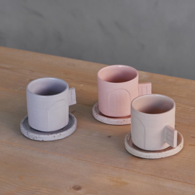 Três canecas de cerâmica pastel com suportes redondos manchados sobre mesa de madeira