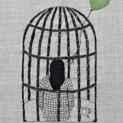Bordado de pessoa dentro de gaiola com balão verde e chávena sobre pano de linho