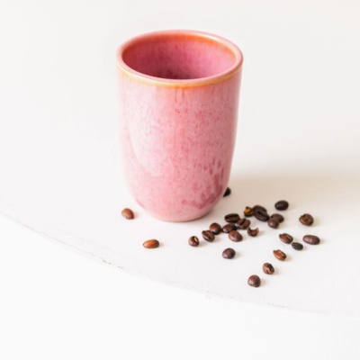 Caneca rosa e grãos de café sobre mesa branca
