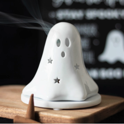 Incense burner em forma de fantasma branco com recortes de estrelas e olhos em cima de tábua de madeira