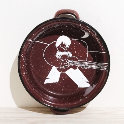 Tabuleiro redondo de metal vermelho escuro com figura pintada a branco e duas pegas.