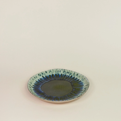 Prato de cerâmica azul e verde com padrão iridescente em fundo bege