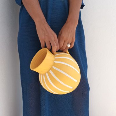 Pessoa segura vaso amarelo de cerâmica com padrão branco, vestindo roupa azul