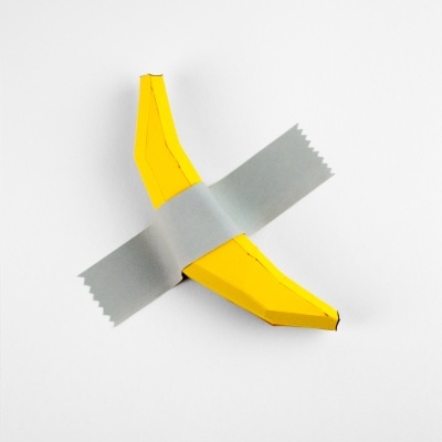 Banana amarela de papel presa com fita prateada numa parede branca