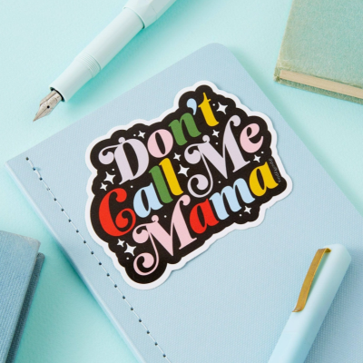 Caderno azul claro com autocolante colorido 'Don't Call Me Mama' e duas canetas sobre uma superfície azul claro