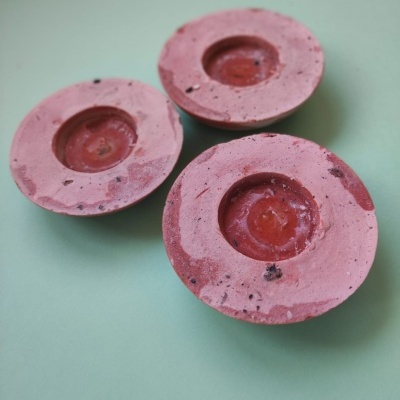 Três velas rosa com manchas castanhas em fundo verde claro.