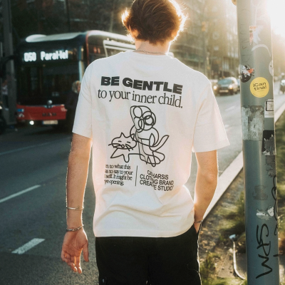 Pessoa de costas a usar t-shirt branca com estampa preta e texto em ambiente urbano com autocarro