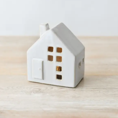 Miniatura branca de casa em cerâmica com janelas e porta recortadas sobre mesa de madeira