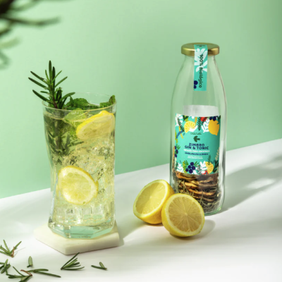 Frasco de Gin & Tonic, copo com bebida e fatias de limão e alecrim, fundo verde claro.