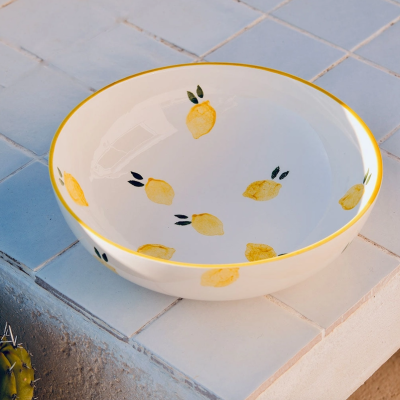 Taça de cerâmica branca com limões amarelos e folhas, borda amarela, sobre azulejos brancos