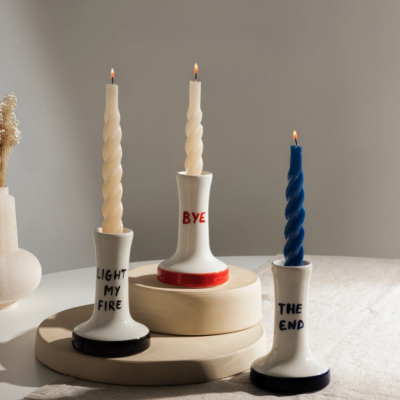 Três castiçais em cerâmica com velas retorcidas acesas e textos visíveis