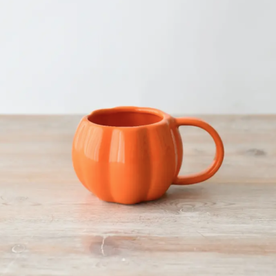 Caneca laranja em forma de abóbora sobre superfície de madeira clara