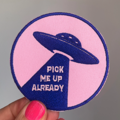 Emblema redondo rosa com disco voador azul e texto branco