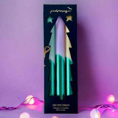 Caixa preta com velas verdes e brancas em forma de árvore de Natal com texto dourado, sobre fundo rosa com luzes decorativas.