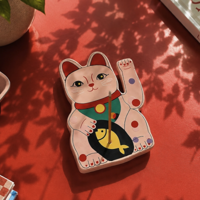 Incensário de cerâmica em forma de gato da sorte colorido sobre superfície vermelha