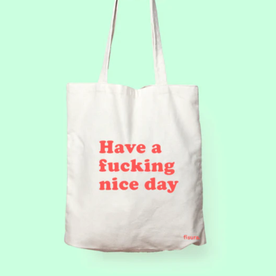 Saco tote branco com texto vermelho 'Have a fucking nice day' e marca 'fisura' num fundo verde claro.