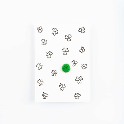 Bloco de notas branco com desenhos de trevos pretos e botão verde no centro.