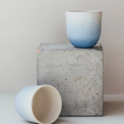 Dois copos de cerâmica azul e branco sobre e ao lado de cubo de cimento cinza