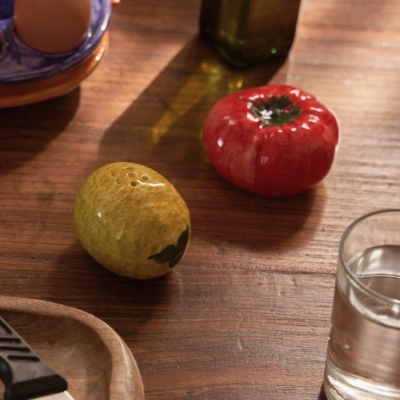 Tempero em forma de limão e tomate em cerâmica sobre mesa de madeira com faca, copo de água, ovos e garrafa