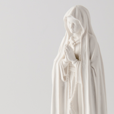 Escultura branca de figura feminina em oração com manto e rosário