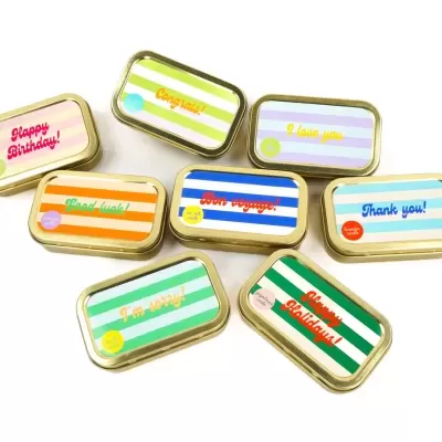 Oito latas pequenas retangulares com tampas coloridas e mensagens em inglês