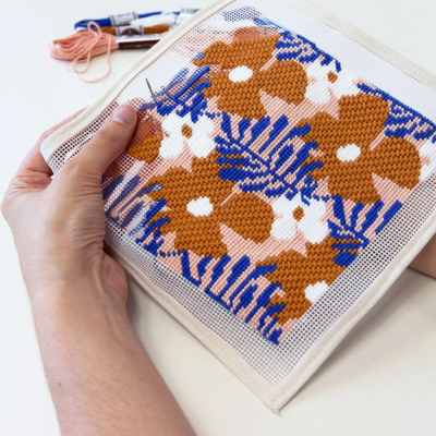 Bordado em tela aida com flores castanhas e folhas azuis nas mãos