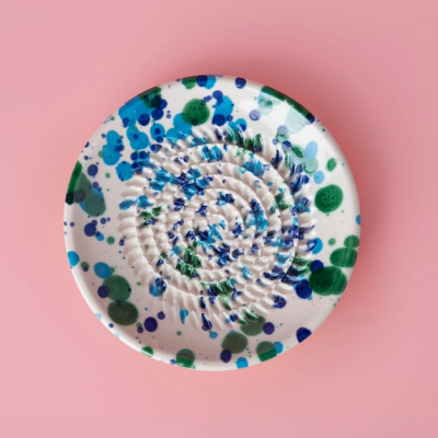 Prato de cerâmica redondo com padrões azuis e verdes sobre superfície rosa
