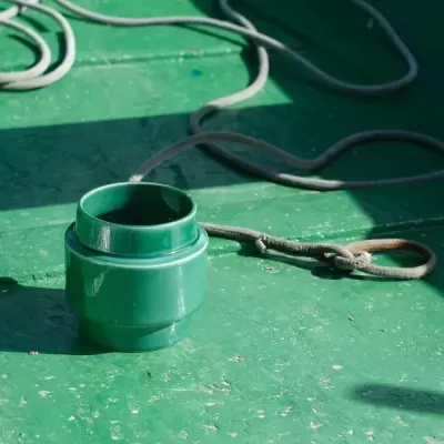 Vaso verde de cerâmica com corda ao lado em superfície verde