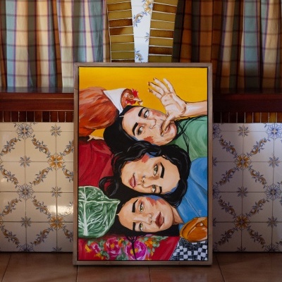 quadro com pintura colorida de três rostos femininos, galinha e elementos naturais junto a azulejos decorativos