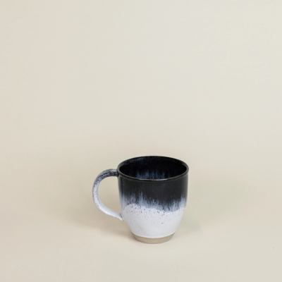 Caneca cerâmica preta e branca com asa, sobre superfície bege
