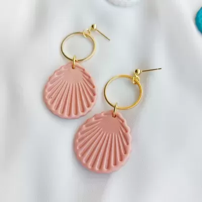 Brincos com argola dourada e pendente de concha rosa sobre fundo branco