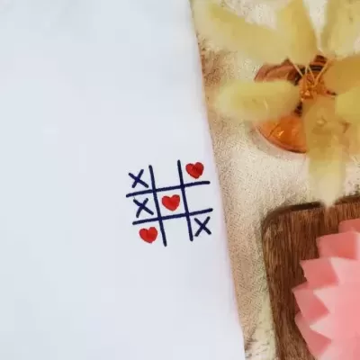 Camisa branca com bordado de jogo da velha com corações vermelhos e X azuis