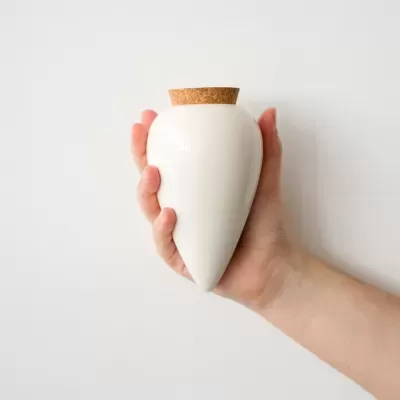 Frasco de cerâmica branco com tampa de cortiça segurado por uma mão