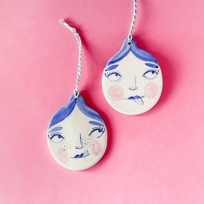 Pendentes de cerâmica com rostos desenhados em fundo rosa