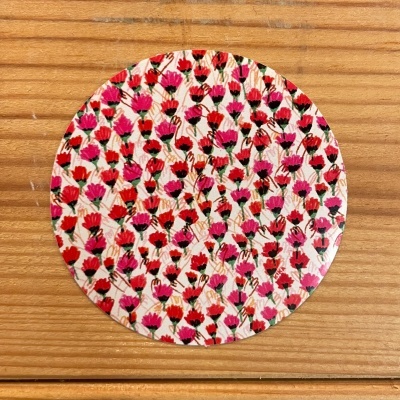 Disco circular com padrão de pequenas flores cor-de-rosa e vermelhas sobre mesa de madeira.