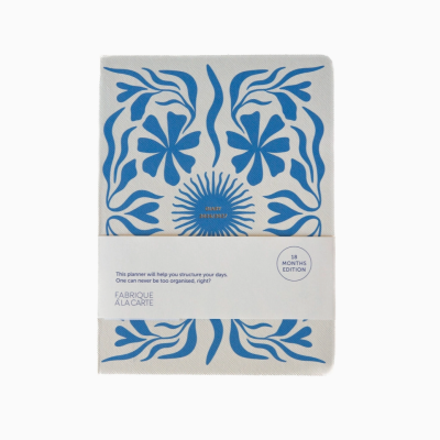 Diário capa tecido bege com padrão azul e texto dourado, faixa branca com texto e selo 18 meses.