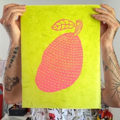 Cartaz de papel verde fluorescente com ilustração cor-de-rosa de uma manga, segurado por pessoa com tatuagens e camisa floral.