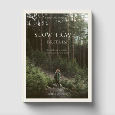 Capa de livro com pessoa a caminhar numa floresta, título SLOW TRAVEL BRITAIN e texto editorial.