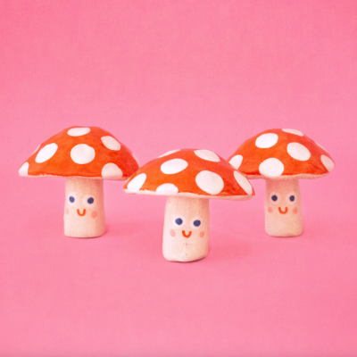 Três cogumelos decorativos com rosto sorridente em fundo rosa