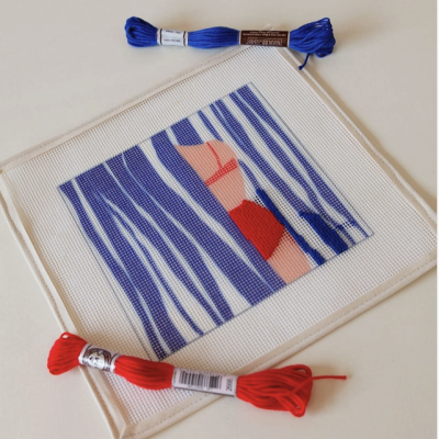 Tecido branco com bordado de mulher em biquíni vermelho e riscas azuis, com novelos de linha azul e vermelho